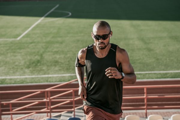 Male athlete in sunglasses and earphones running up the stairs of a stadium